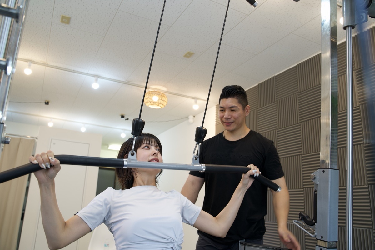 パーソナルジムでウェイトトレーニングを行う女性とトレーナー