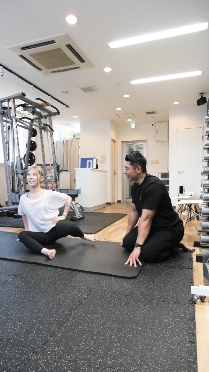 マットの上でお尻まわりのストレッチを行う女性とトレーナー