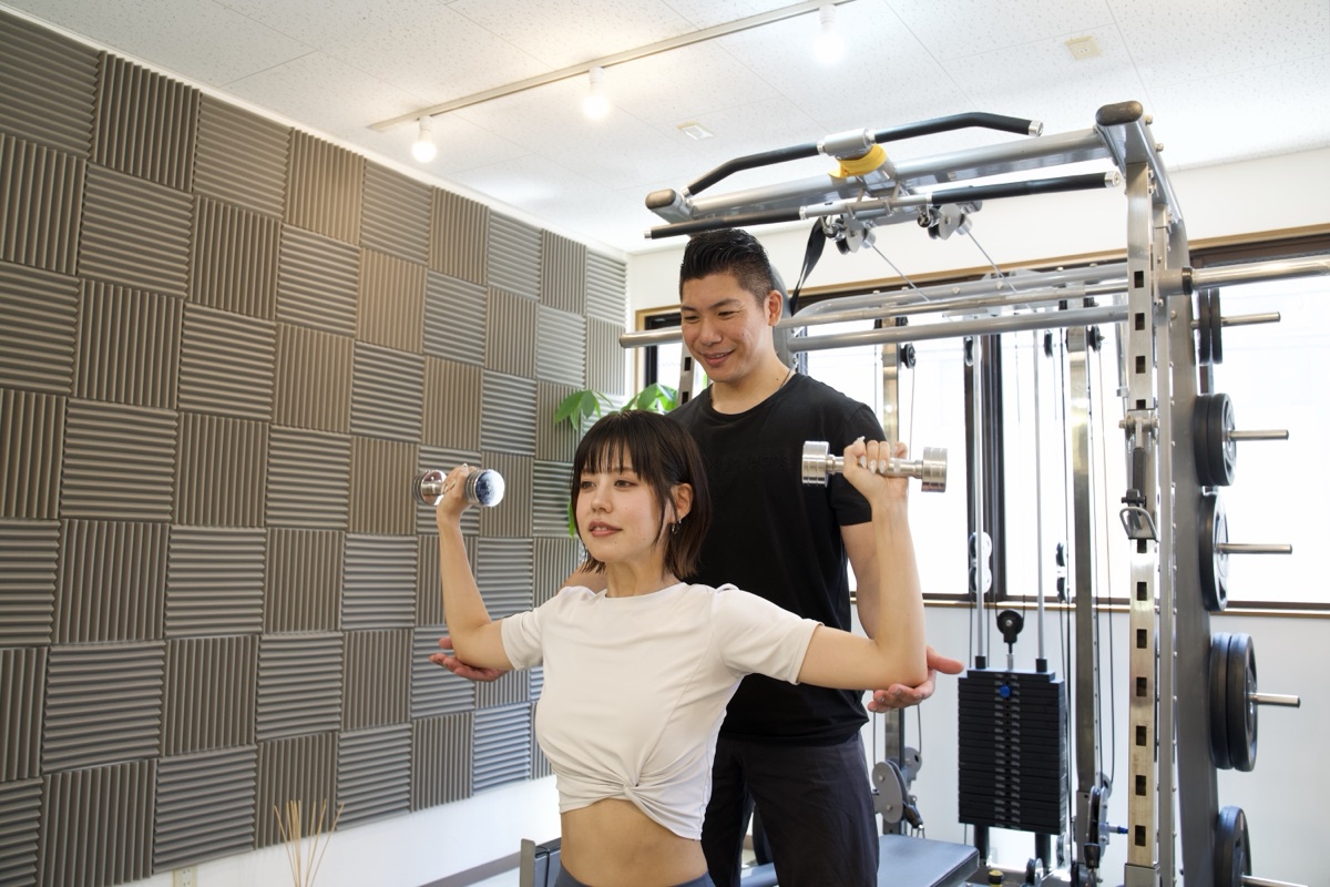 完全個室のパーソナルジムでダンベルトレーニングの指導を受ける女性