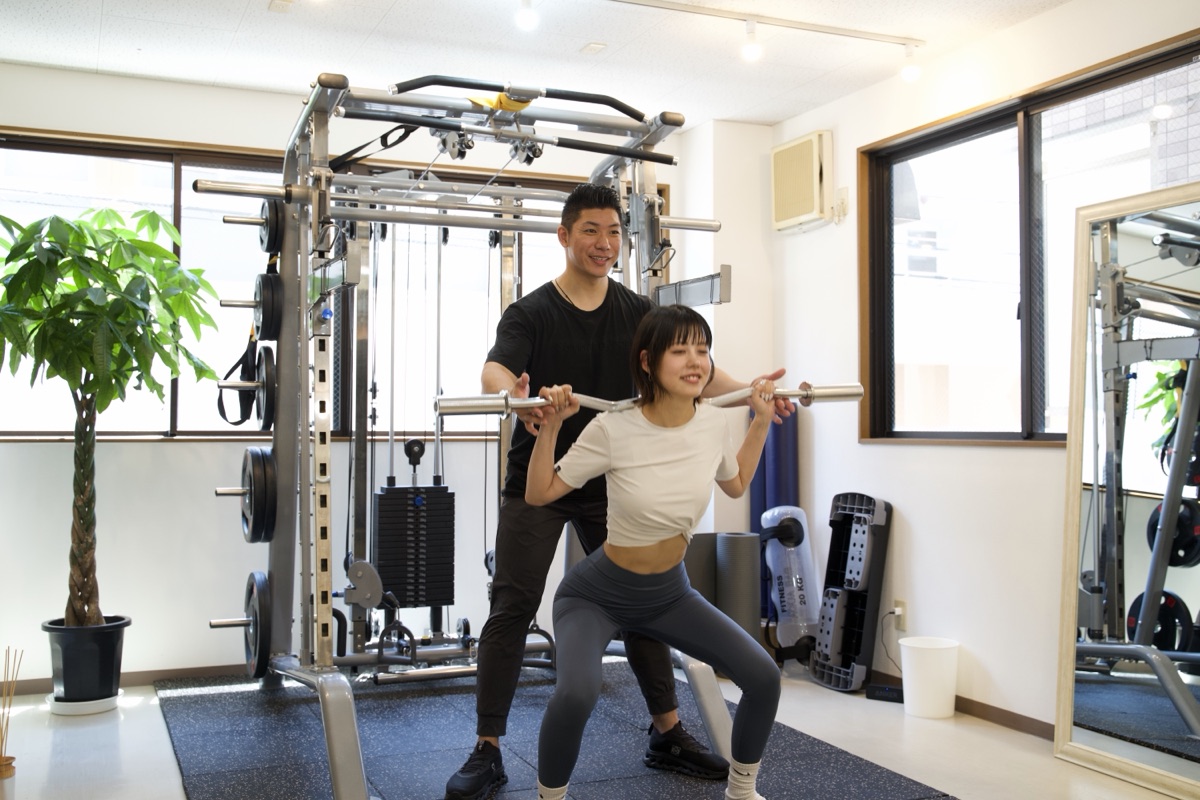 冷え性改善のために下半身の筋トレ(スクワット)を行う女性とトレーナー