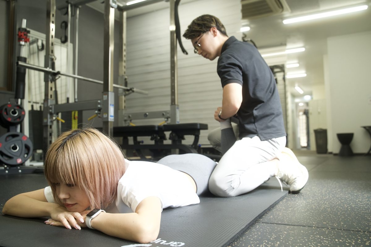 灘駅店でトレーナーのサポートを受けながら脚のストレッチをする女性