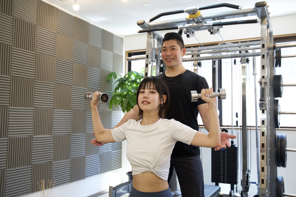 甲子園口のパーソナルジムでトレーナーと一緒にダンベルトレーニングをする運動初心者の女性
