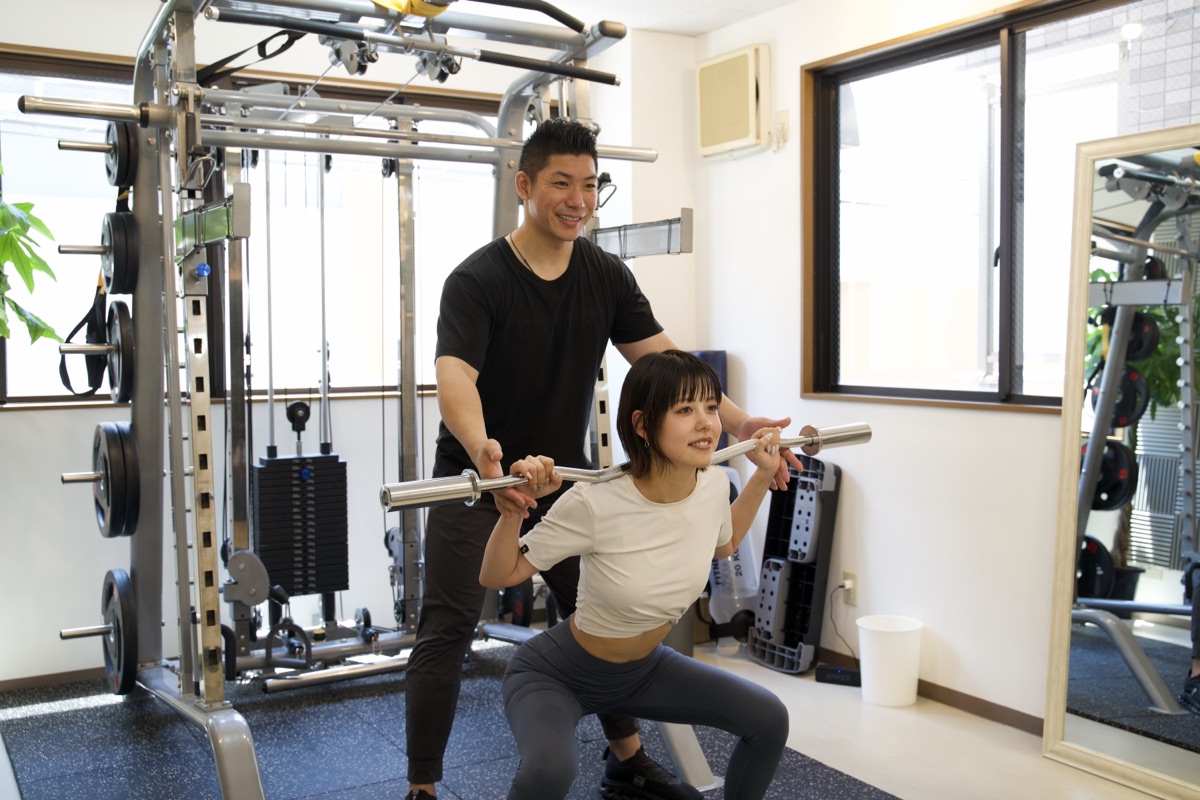 トレーナーの補助でスクワットを行う女性
