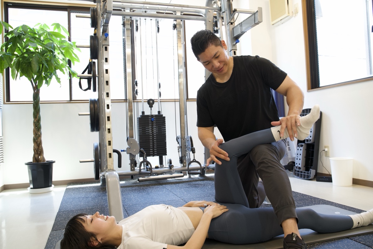 トレーナーが女性の脚のストレッチをサポートする様子