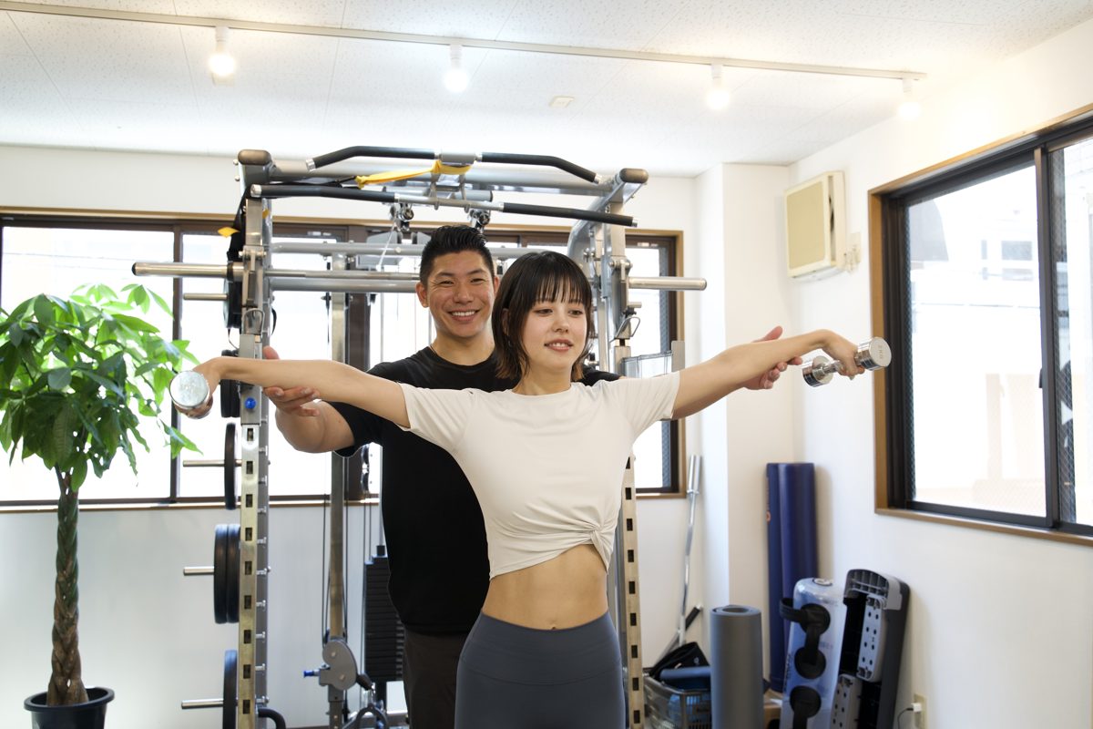 胸を開いて肩甲骨を寄せるトレーニングで巻き肩を改善する女性とトレーナー