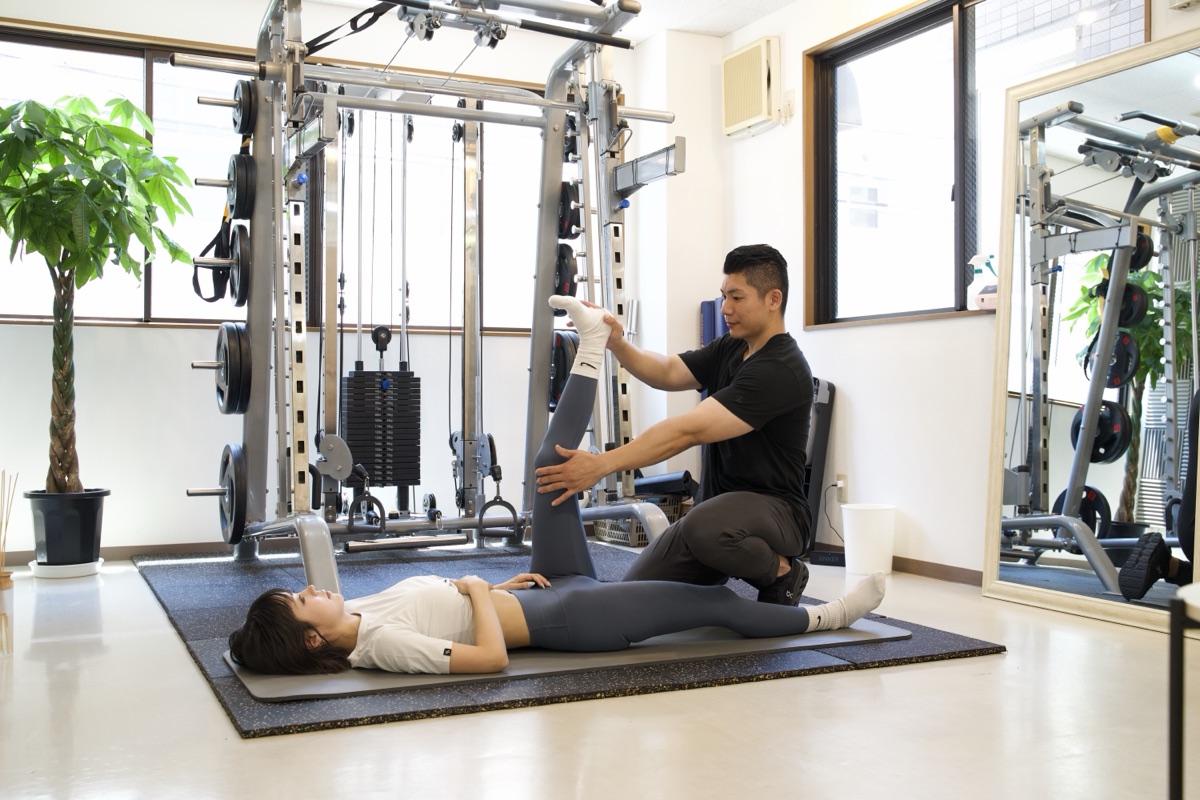 座り仕事で固まりやすい股関節を、トレーナーがマットの上で補助しながら伸ばしている様子