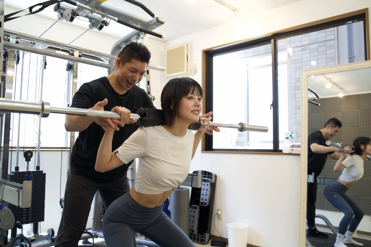 トレーナーの補助でスクワットを行う女性
