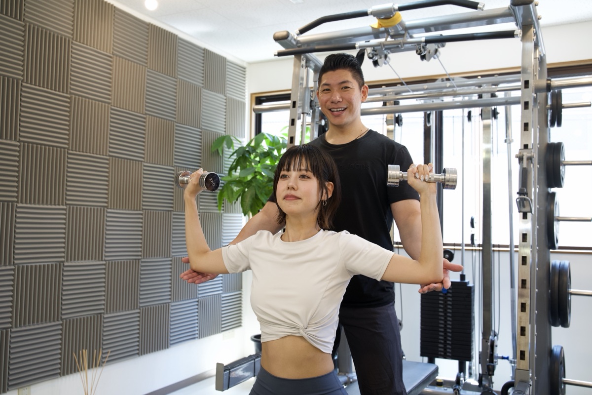 ウェディングドレスに向けて肩や二の腕をダンベルで鍛える女性とトレーナー