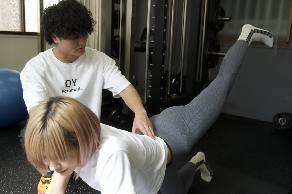 トレーナーの指導で四つ這いになり脚を後ろに上げるお尻のトレーニング